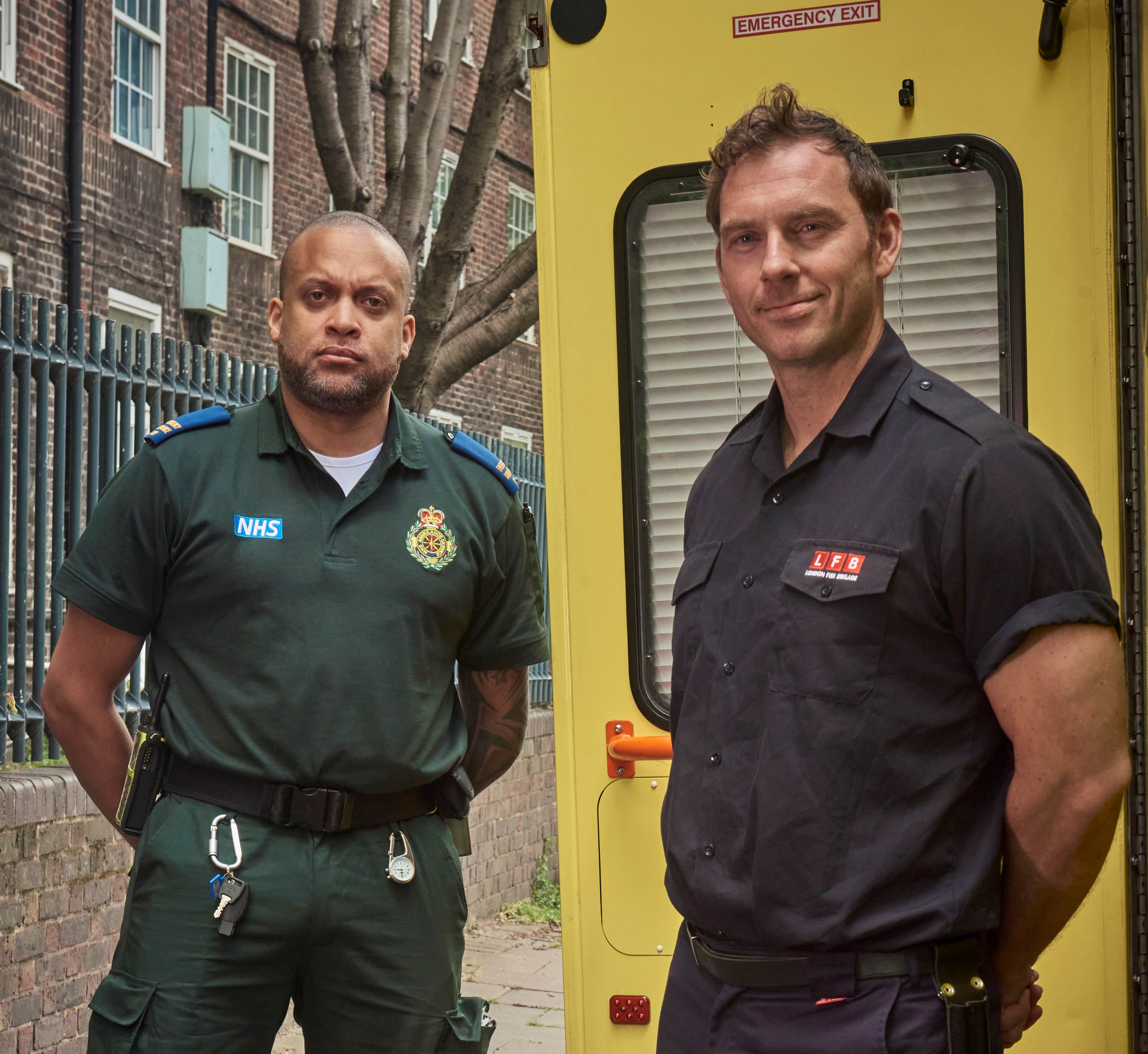NHS ambulance paramedic and London Fire Brigade officer standing together on pavement.