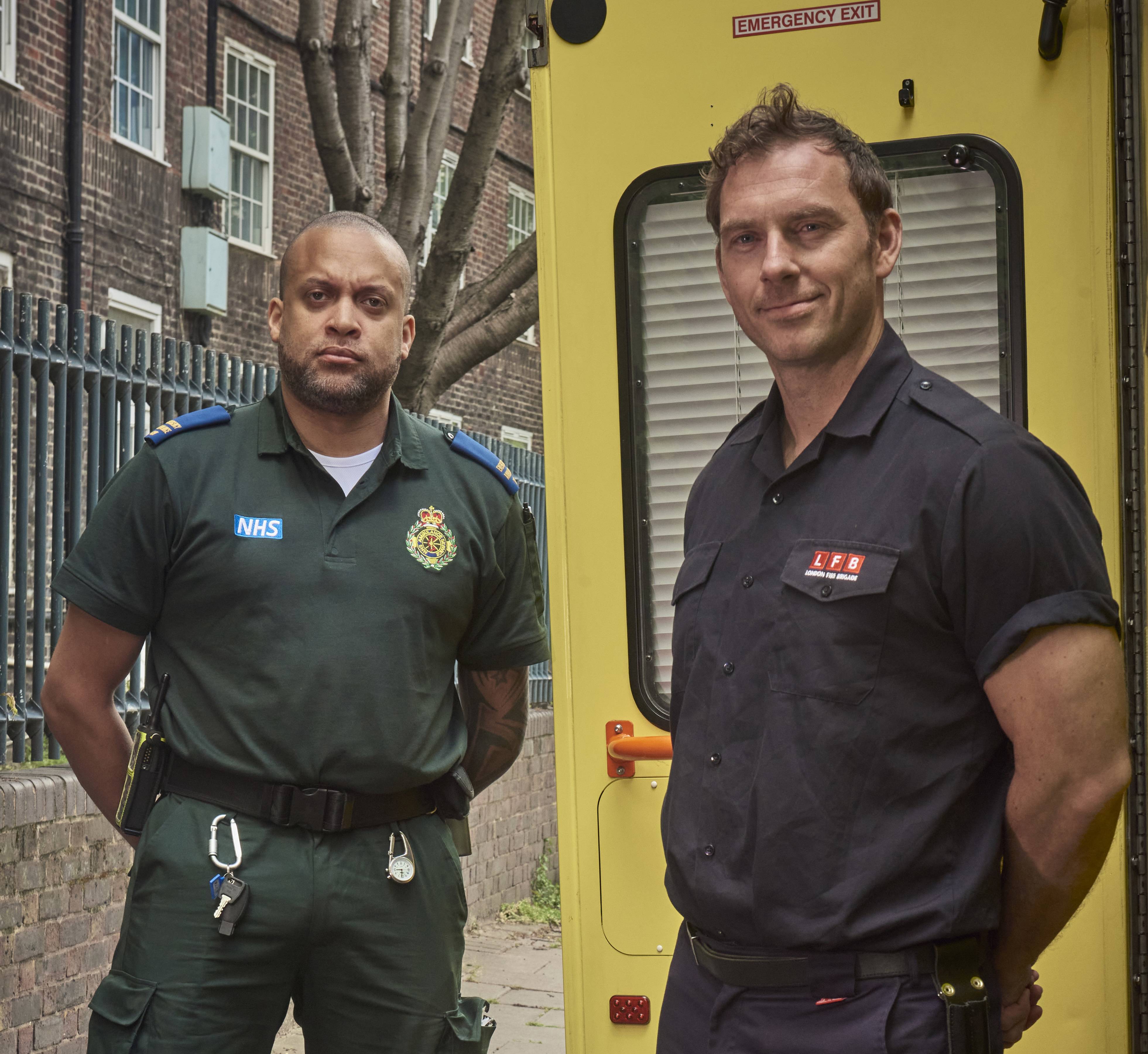 NHS ambulance paramedic and London Fire Brigade officer standing together on pavement.