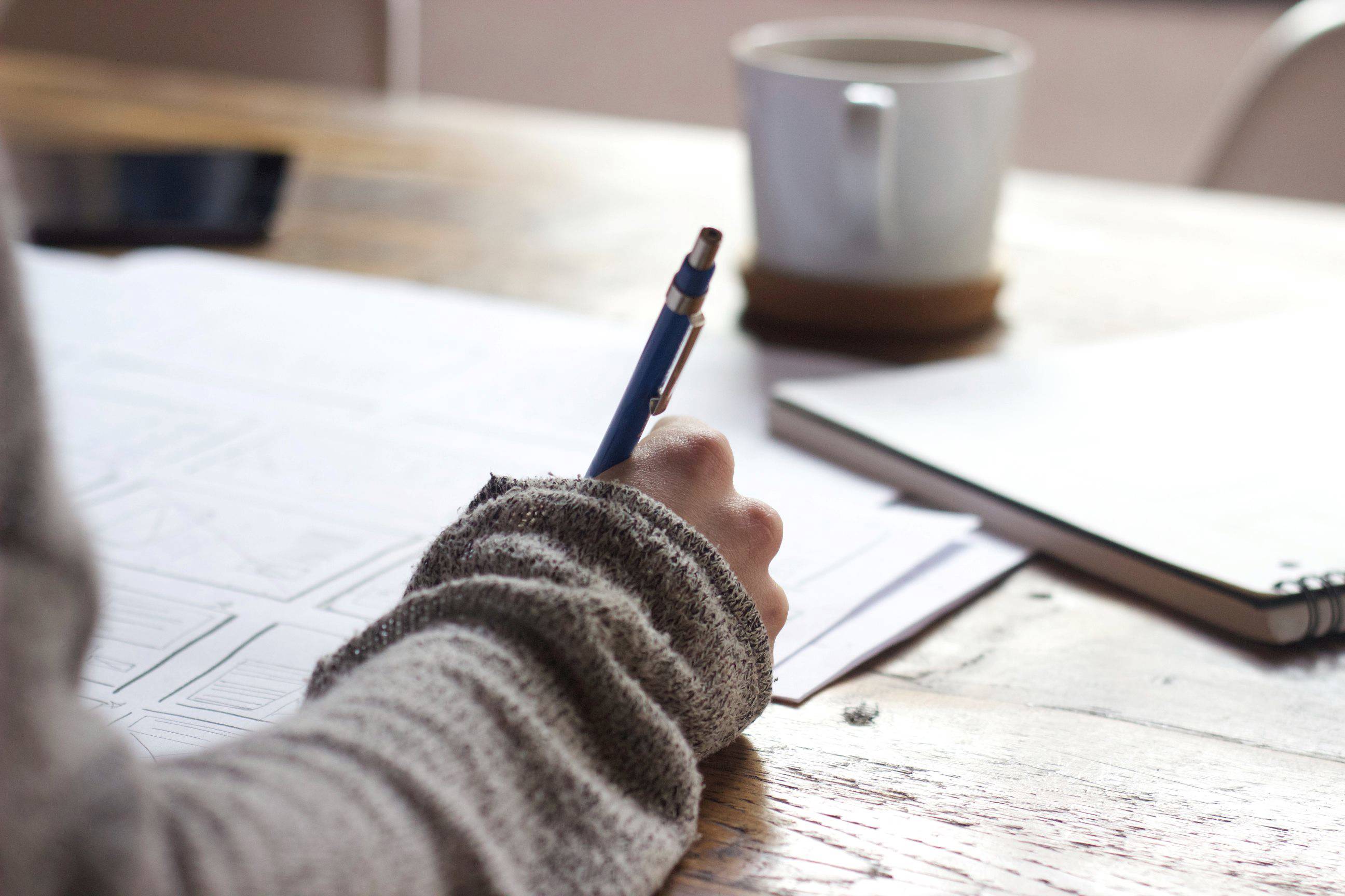 Person writing on paper worksheets with a cup of tea