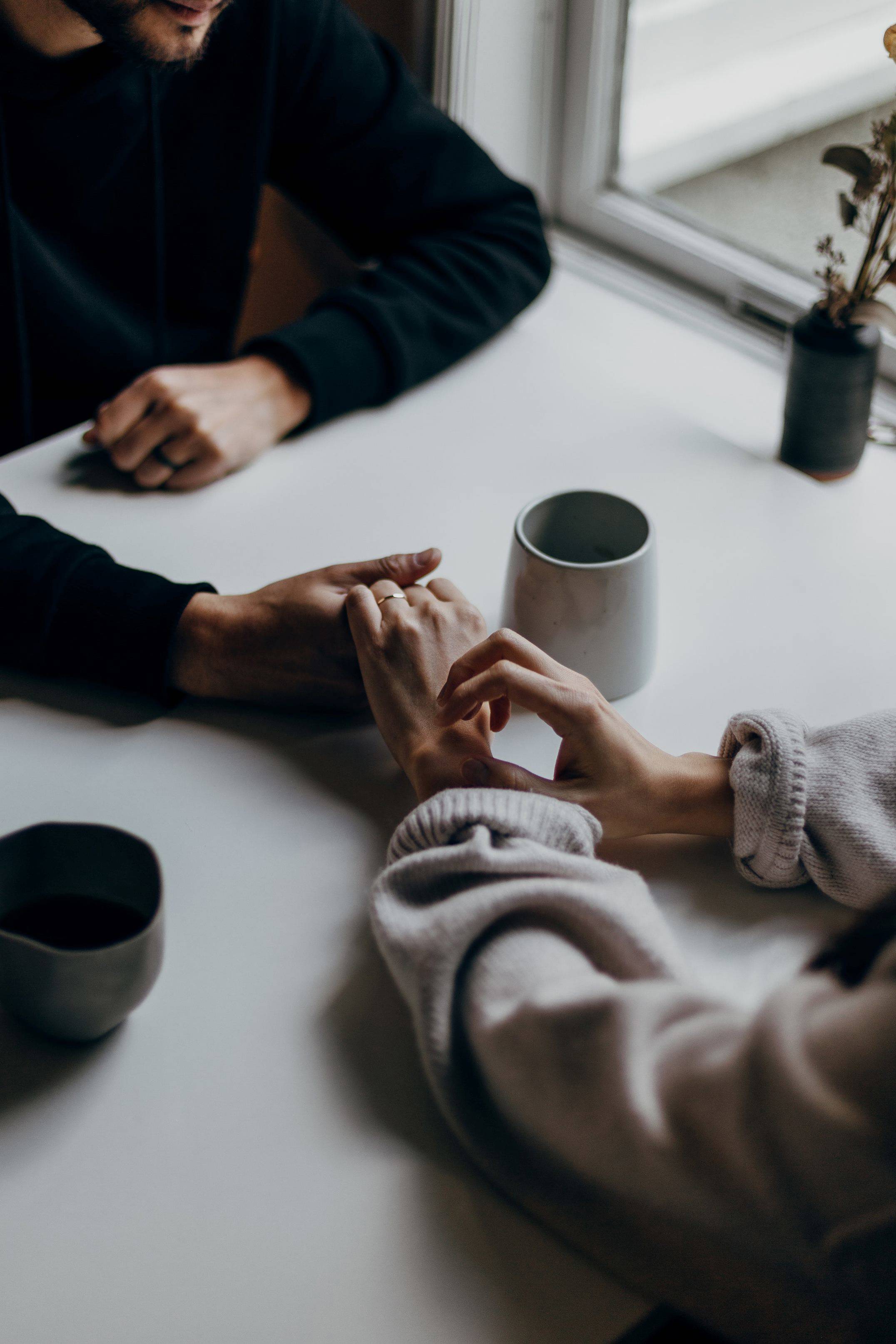 Two people holding hands over a white table with a cup tea next to them