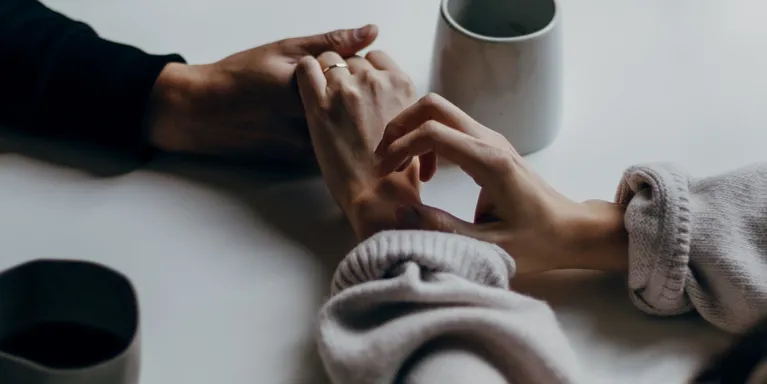Two people holding hands over a white table with a cup tea next to them Two people holding hands over a white table with a cup tea next to them