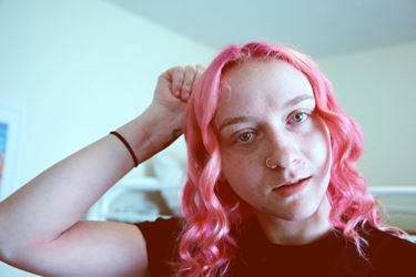 Person with pink hair and wrist tattoo staring at camera