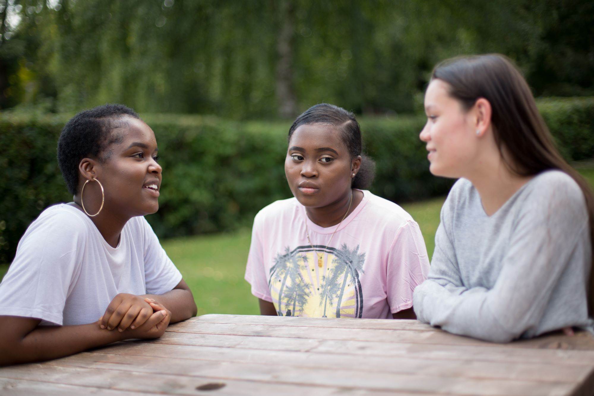 3 young people sat at a picnic table talking.