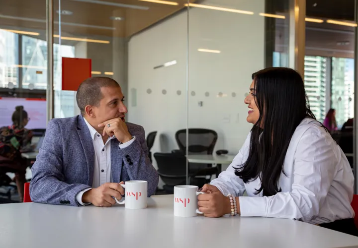 Two people in an office talking over two mugs with WSP branding.