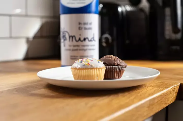Cakes on a kitchen surface, with a Mind fundraising collection tin behind.
