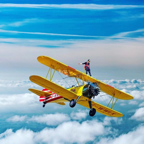 Person standing on top of flying yellow plane.