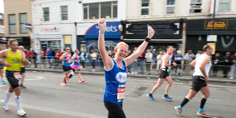 woman running in race wearing mind top and cheering with arms in air woman running in race wearing mind top and cheering with arms in air
