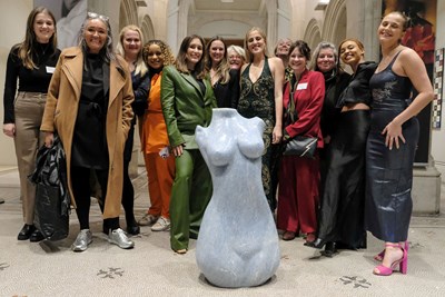 Group of event attendees standing around the artwork, a sculpture of a woman's body