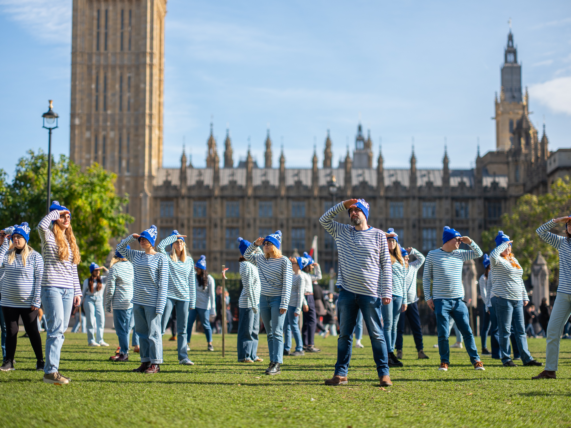 Campaigners in stripey shirts and blue bobble hats outside parliament. They are looking around as though searching for something.