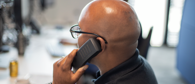 Black man with glasses facing away from camera, holding a phone to his ear. 