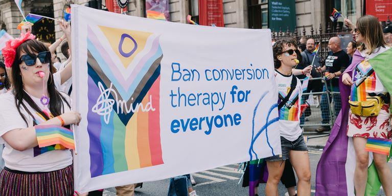 Mind volunteers carrying banner at London Pride saying 'Ban conversion therapy for everyone.'