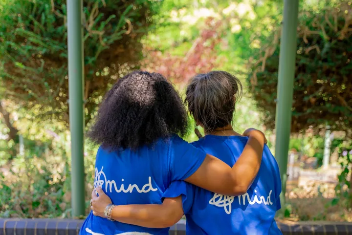 The backs of two women in Mind tshirts, hugging arm in arm.