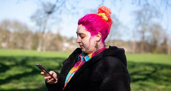 Person with pink hair in park checking phone